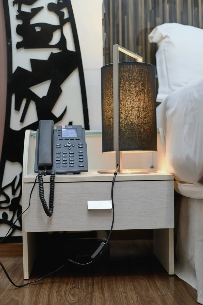 Bedside lamp and phone beside a carved black screen with African motifs