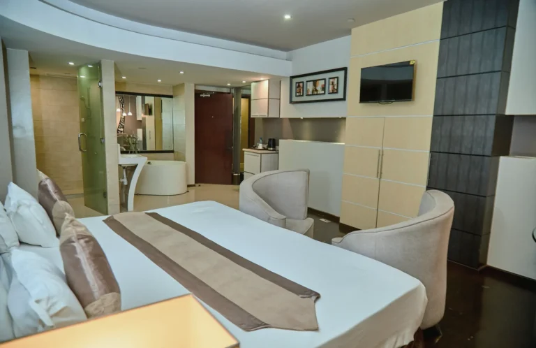 Executive suite with a king bed, lounge chairs and a glass-walled bathroom with a freestanding tub