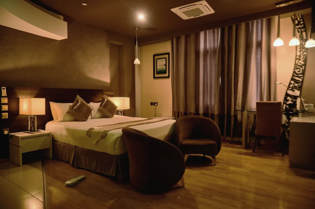 Room at night lit by bedside lamps and pendant lights, with a carved screen by the window