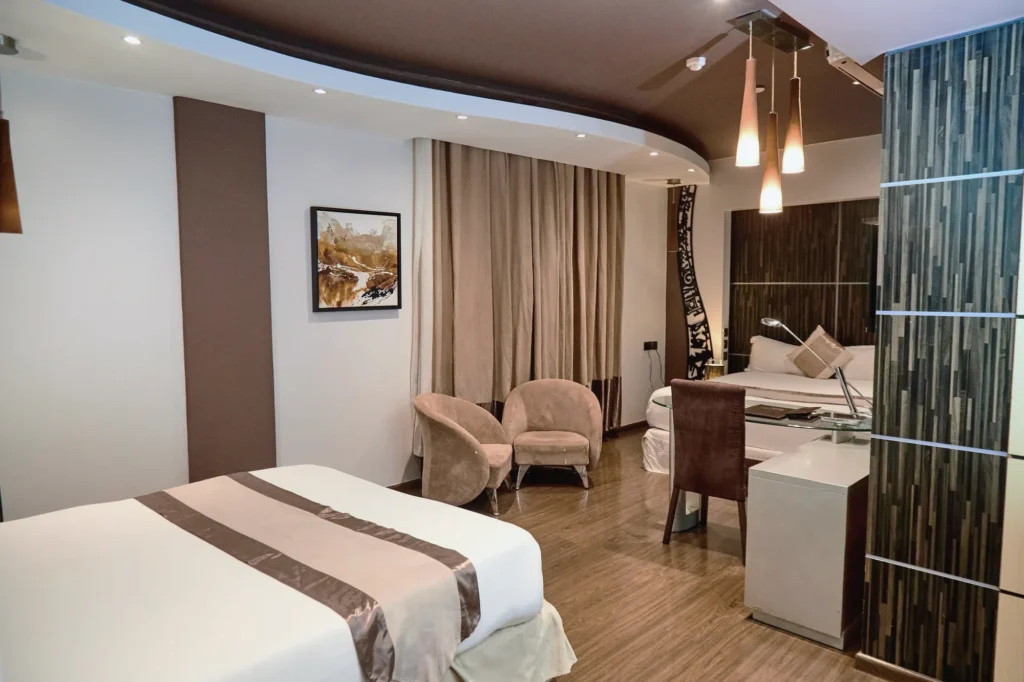 Twin Queen Room with two beds, a bronze bed runner, velvet tub chairs and a writing desk
